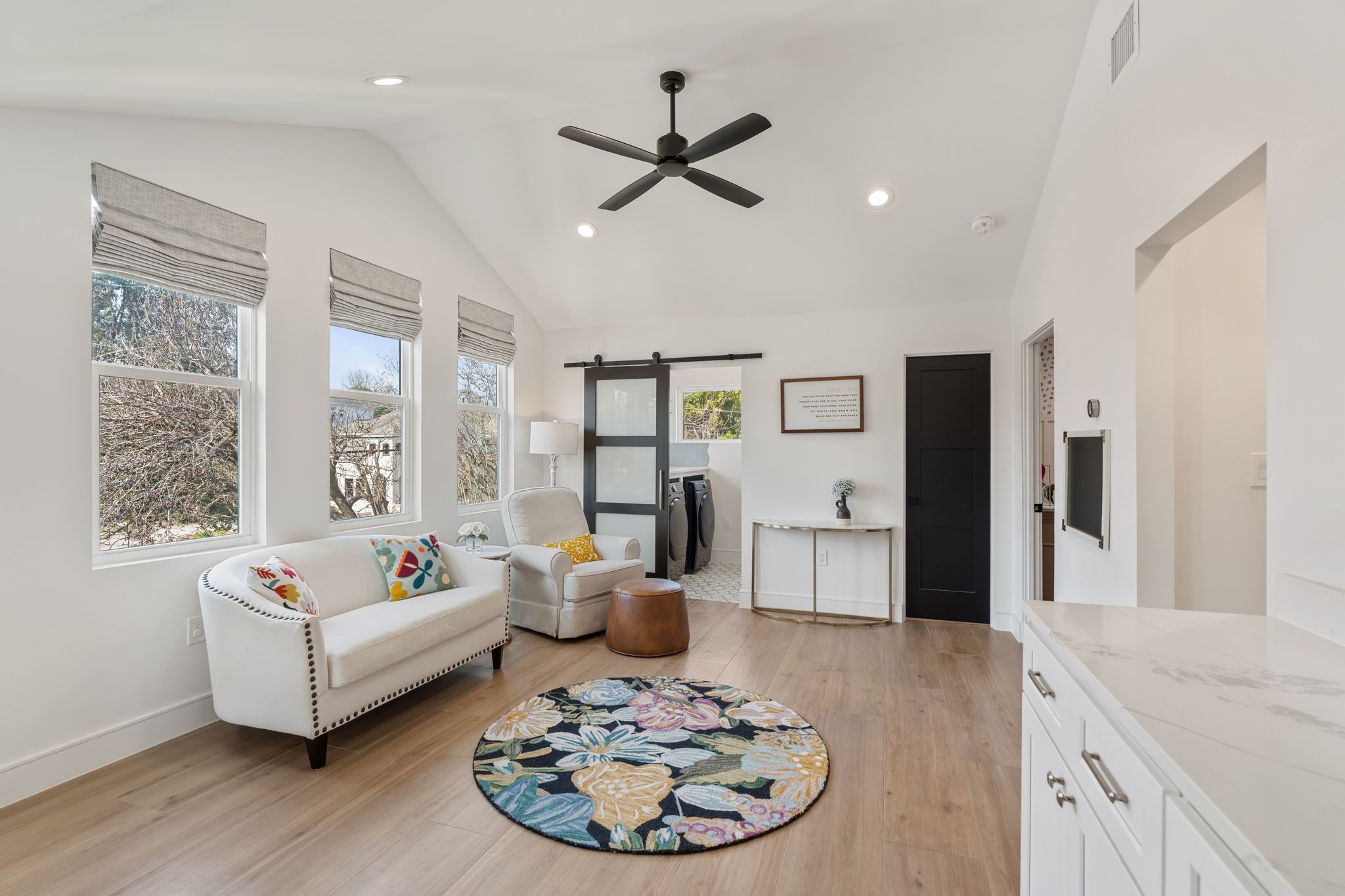 2626 Reagan Street Houston, TX 77009 - Photo 27 of 50 Additional upstairs flex space separates another 2 secondary bedrooms and offers a versatile area that can be used as a second living space, playroom, or reading nook. The room features vaulted ceilings with a modern ceiling fan, recessed lighting, warm wood flooring, and multiple windows with custom blinds that fill the space with natural light. A sliding door leads to the main utility room, thoughtfully located near the upstairs bedrooms for everyday convenience. The door on the right leads to a half bat