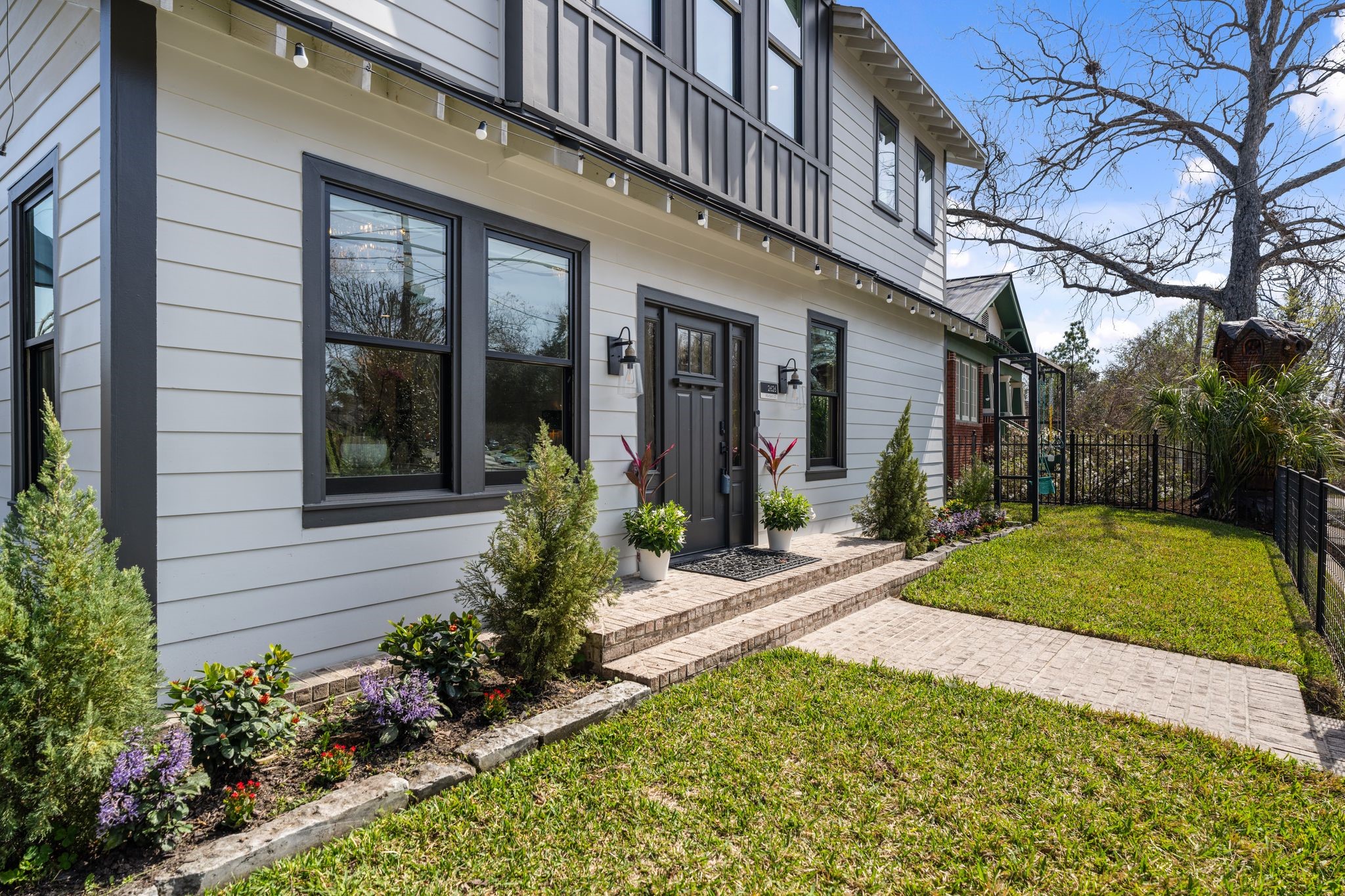 2626 Reagan Street Houston, TX 77009 - Photo 3 of 50 The front exterior showcases a modern farmhouse style facade with a fully fenced front yard offering ample space for kids and puts to play. A brick walkway leads to the front door, complemented by landscaped garden beds and a sprinkler system for easy lawn maintenance. On the side of the yard is a built in swing set!