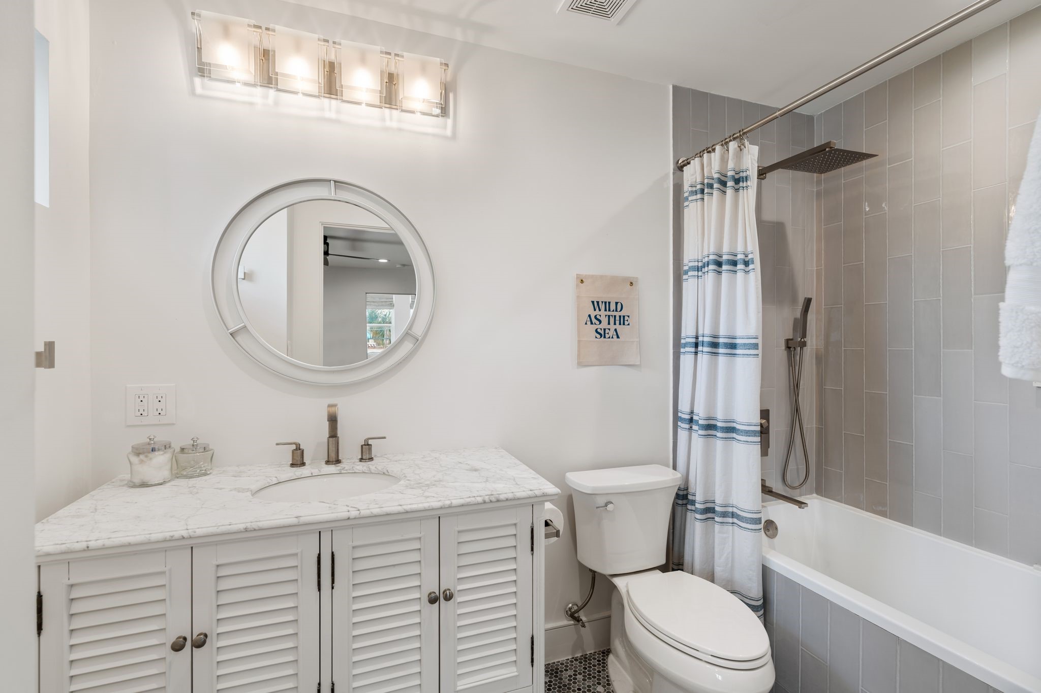 2626 Reagan Street Houston, TX 77009 - Photo 33 of 50 The en-suite bathroom has a marble countertop vanity with cabinet storage, a round framed mirror, and modern vanity lighting. The tub/shower combination includes large-format tile surround, complemented by a rainfall shower head and a hexagon tile flooring design.