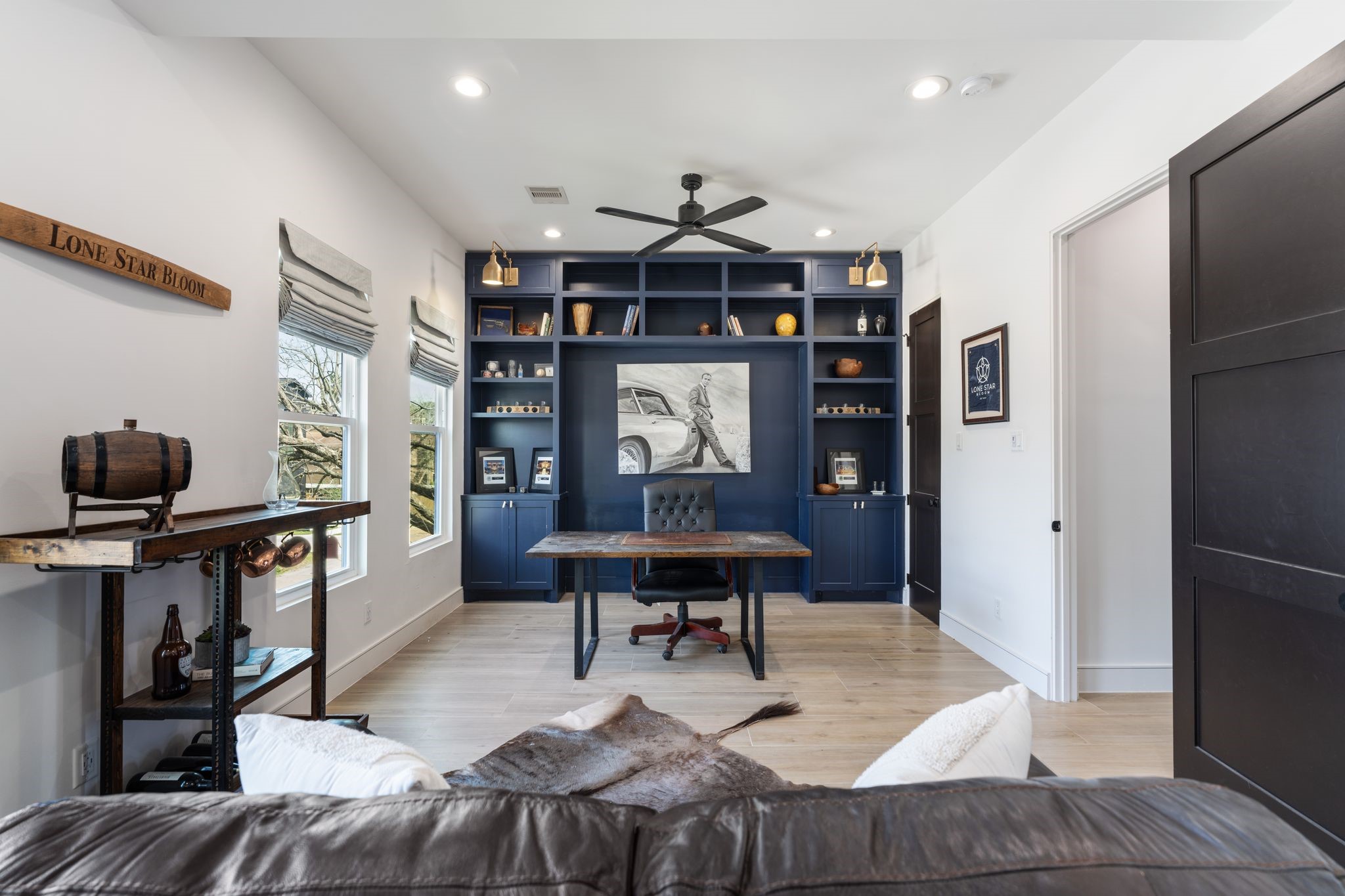 2626 Reagan Street Houston, TX 77009 - Photo 34 of 50 Another spacious upstairs bedroom is currently being used as a home office, featuring multiple windows that bring in abundant natural light. The room also showcases a modern ceiling fan, recessed lighting, and a custom built-in shelving and cabinetry wall with a desk area, offering a flexible space for work, study, or additional living.