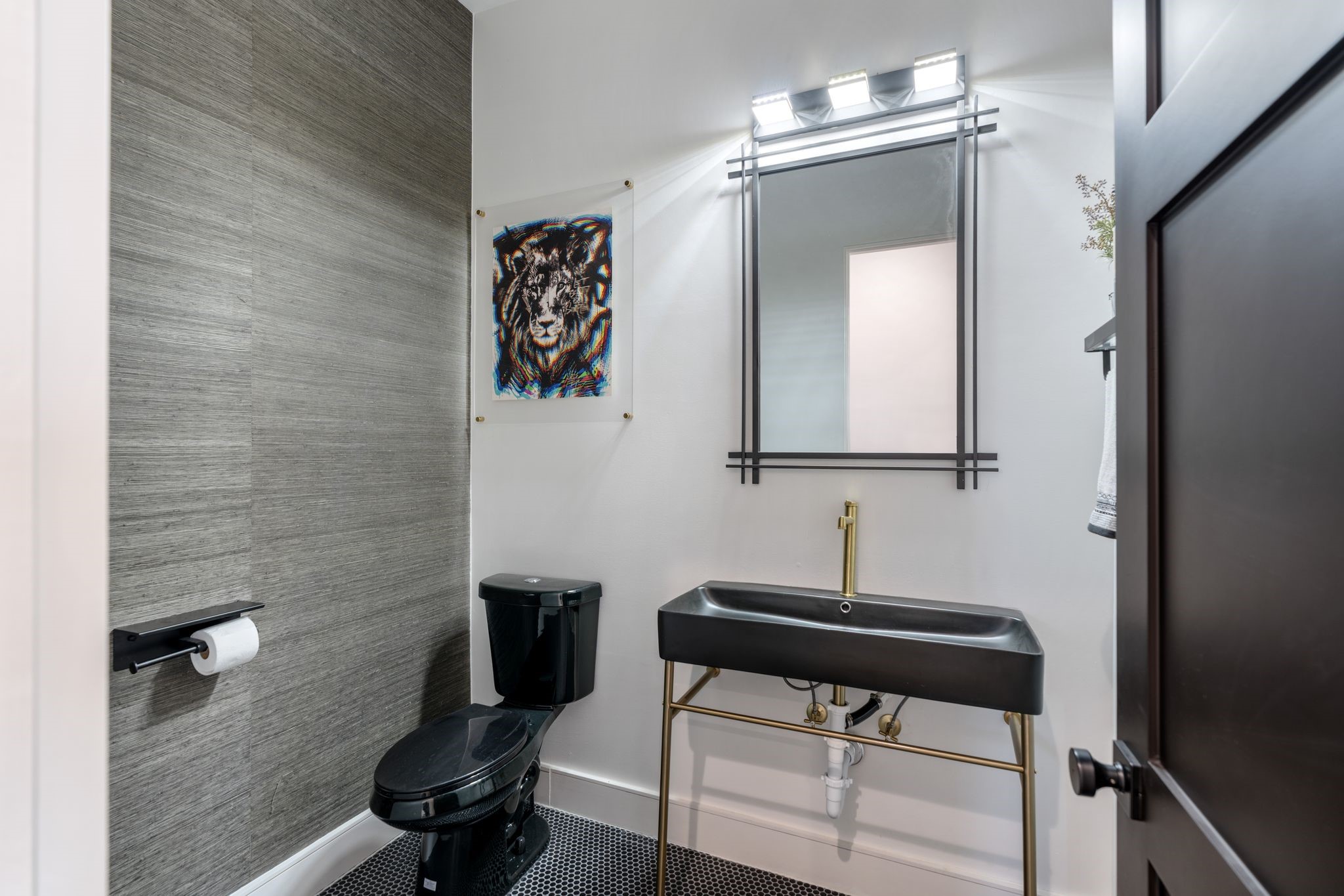 2626 Reagan Street Houston, TX 77009 - Photo 38 of 50 A stylish half bath located just off the game room featuring bold textured wallpaper, a statement black toilet, and black hexagon tile flooring. The space is anchored by an oversized modern black sink with gold fixtures and an industrial style mirror with modern vanity lighting, creating a striking designer look.