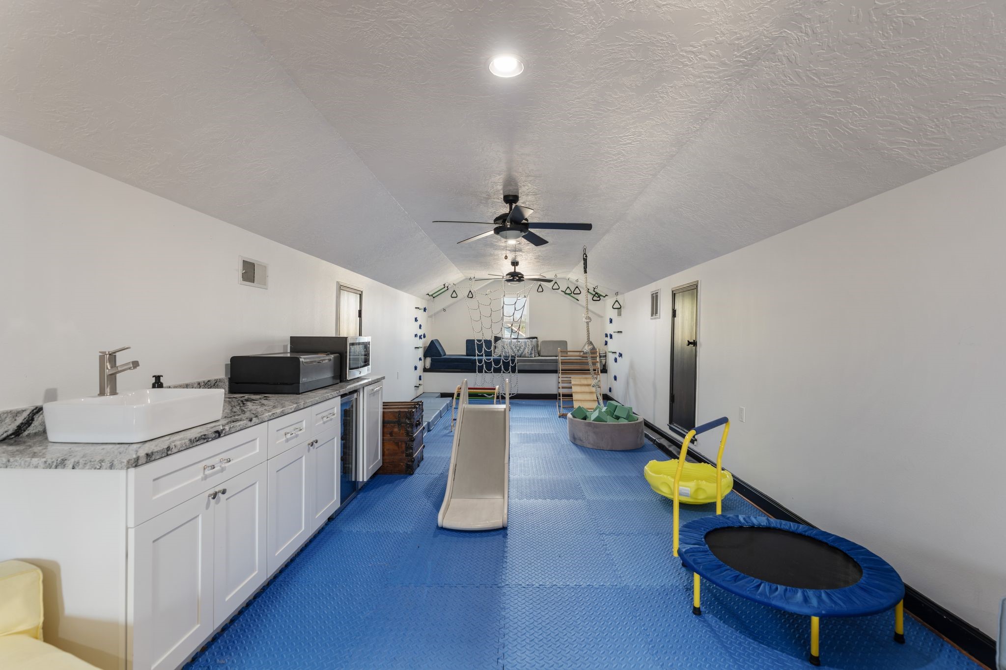 2626 Reagan Street Houston, TX 77009 - Photo 39 of 50 Versatile third floor flex space currently set up as a playroom, offering endless possibilities for use. The room features a built-in bar area with sink, beverage fridge, and storage, along with fun elements like a climbing wall, rope swing, and access to additional floor storage within the attic space.