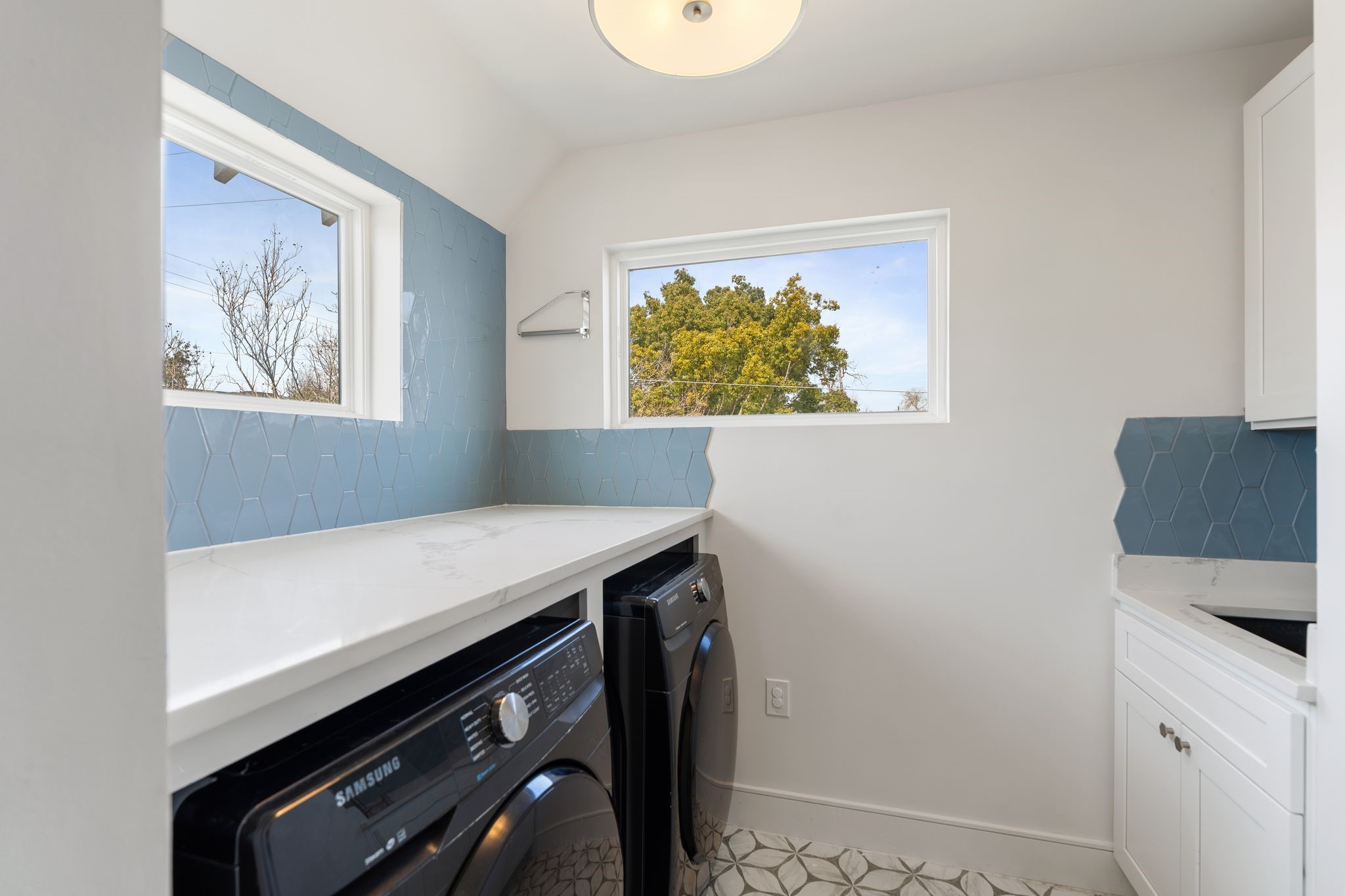 2626 Reagan Street Houston, TX 77009 - Photo 41 of 50 Conveniently located upstairs near all of the bedrooms, this thoughtfully designed utility room features quartz countertops with an extending folding counter, blue tile backsplash, decorative tile flooring, a utility sink with storage below, and windows that bring in tons of natural light.