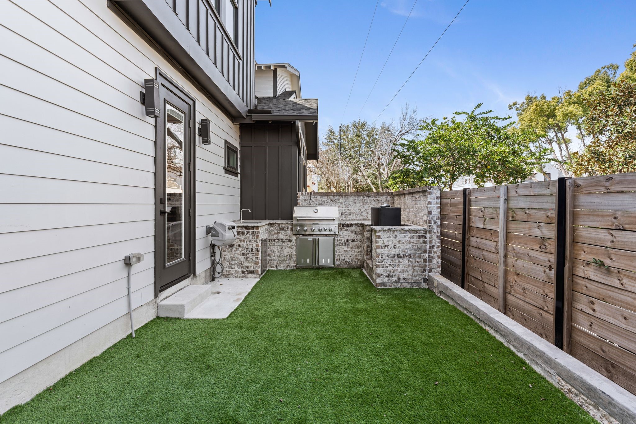 2626 Reagan Street Houston, TX 77009 - Photo 45 of 50 The yard features a built-in outdoor kitchen equipped with a KitchenAid grill, built in smoker, and sink, creating a convenient setup for outdoor cooking and entertaining, while the door shown leads to the additional flex space that connects back into the home and into the main backyard space.