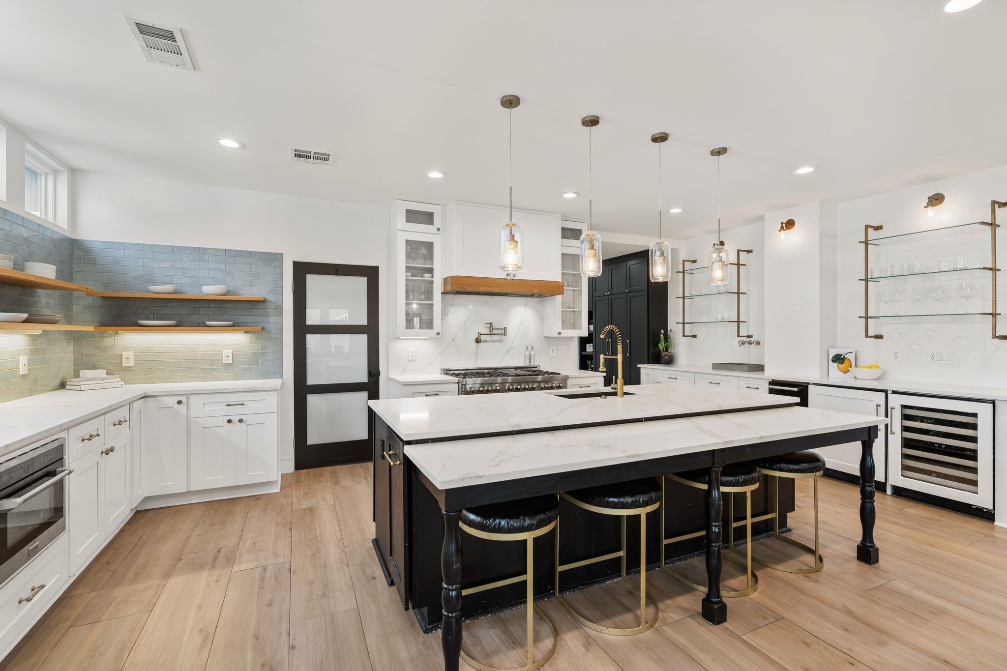 2626 Reagan Street Houston, TX 77009 - Photo 8 of 50 As you walk into the kitchen, you'll notice that no detail was overlooked in the design. The space features quartz countertops, custom cabinetry, designer blue tile backsplash, floating wood display shelves, and under cabinet lighting. A large island with breakfast bar seating is highlighted by gold pendant lighting and convenient pull out trash cans on both sides creating a beautiful and functional centerpiece for the kitchen.