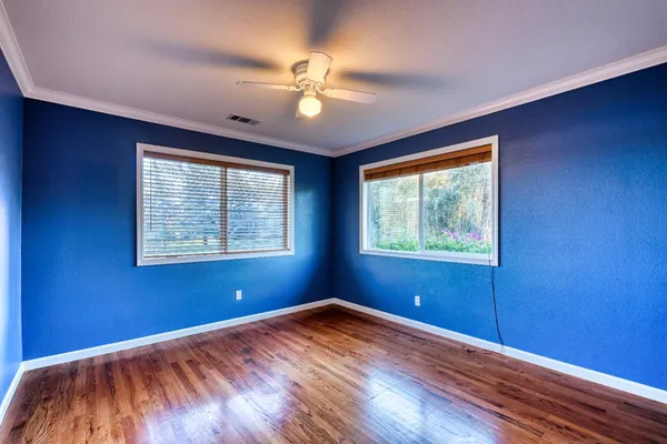an empty room with wooden floor fan and windows