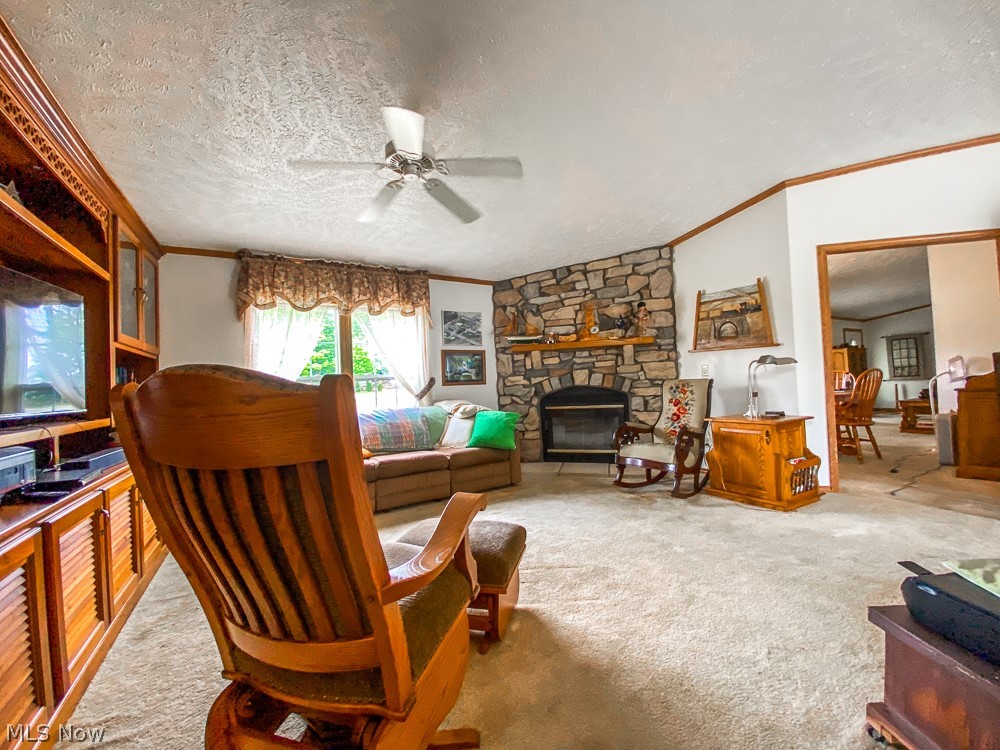17499 Kinsman Road Middlefield, OH 44062 - Photo 17 of 49 Carpeted living room with a textured ceiling, a stone fireplace, crown molding, and ceiling fan