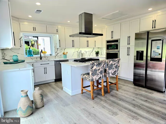 a kitchen with stainless steel appliances kitchen island granite countertop a table chairs refrigerator and microwave