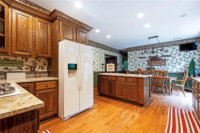 a kitchen with stainless steel appliances granite countertop a refrigerator a stove top oven and a dining table with wooden floor