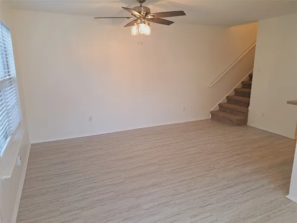 a view of an empty room with wooden floor and a ceiling fan