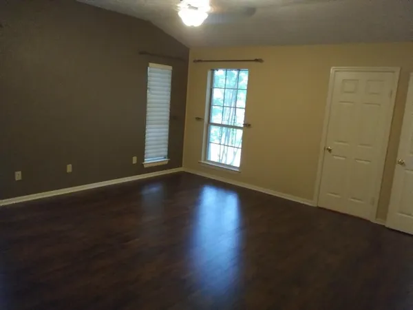 an empty room with wooden floor and windows with curtains