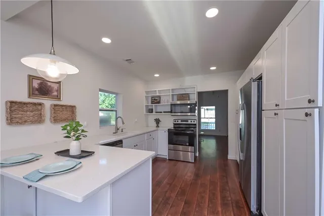 a kitchen with stainless steel appliances kitchen island granite countertop a refrigerator a stove a sink dishwasher and a dining table with wooden floor