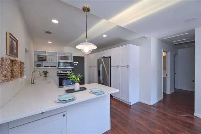a kitchen with stainless steel appliances kitchen island granite countertop a refrigerator a sink and a wooden floor