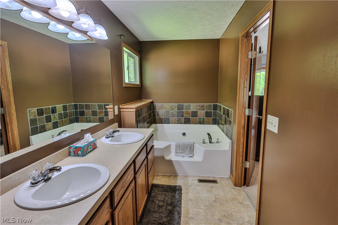 11154 Johnsford Road Southwest Beach City, OH 44608 - Photo 33 of 50 Bathroom featuring a dual vanity with laminate countertops, a large mirror, and a built-in jetted tub with tile surround