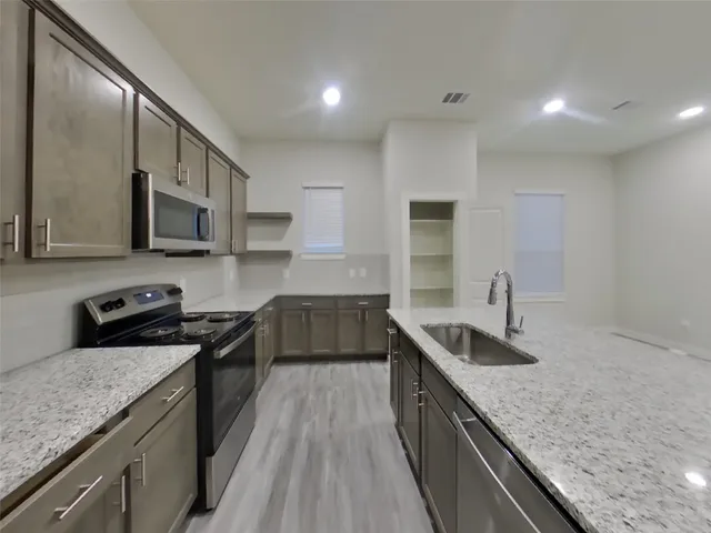 a kitchen with granite countertop stainless steel appliances a sink a stove top oven a counter space and cabinets