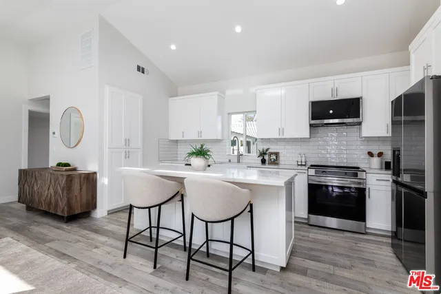 a kitchen with stainless steel appliances granite countertop a stove a sink a microwave a refrigerator and white cabinets