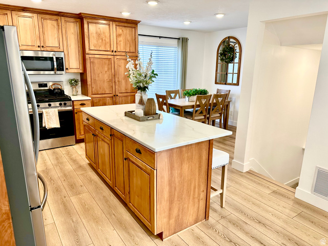 7818 North Windhover Road Eagle Mountain, UT 84005 - Photo 9 of 32 Kitchen featuring a large central island with a light-colored countertop, rich wood cabinetry, stainless steel appliances, wood-finish flooring, and recessed lighting