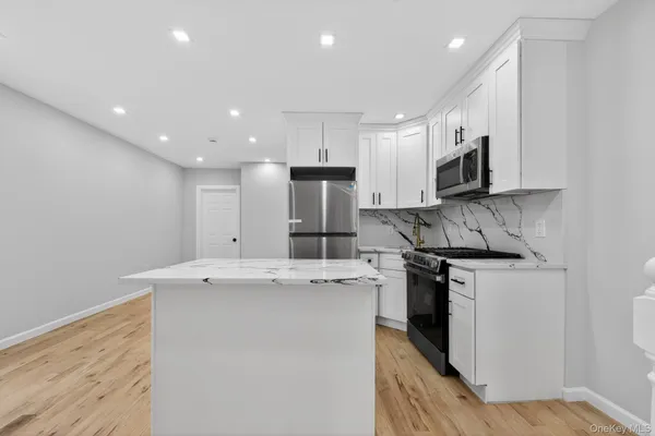 a large kitchen with stainless steel appliances granite countertop a stove a sink a refrigerator and white cabinets with wooden floor