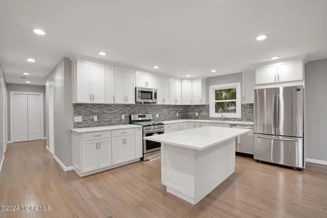 a large kitchen with stainless steel appliances granite countertop a stove a sink dishwasher a refrigerator and white cabinets with wooden floor