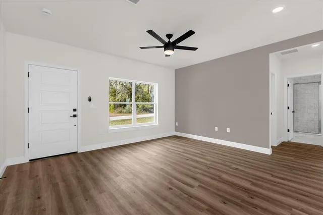 a view of a big room with wooden floor a ceiling fan and windows