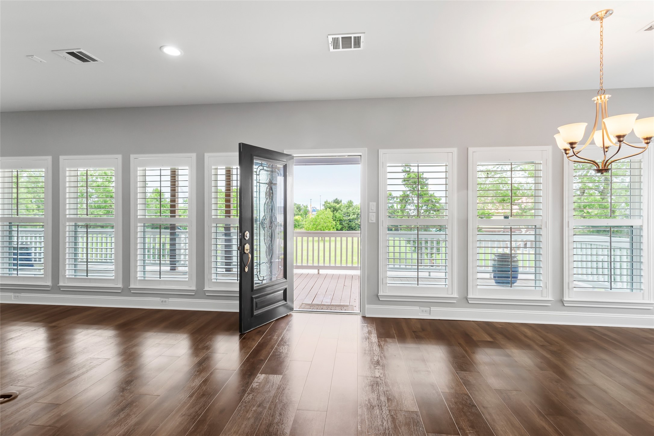 610 South Shady Lane La Porte, TX 77571 - Photo 11 of 50 This spacious room features elegant wood laminate flooring, abundant natural light from multiple windows with shutters, and a stylish chandelier. The open door leads to a deck with a serene view of greenery, enhancing indoor-outdoor living.