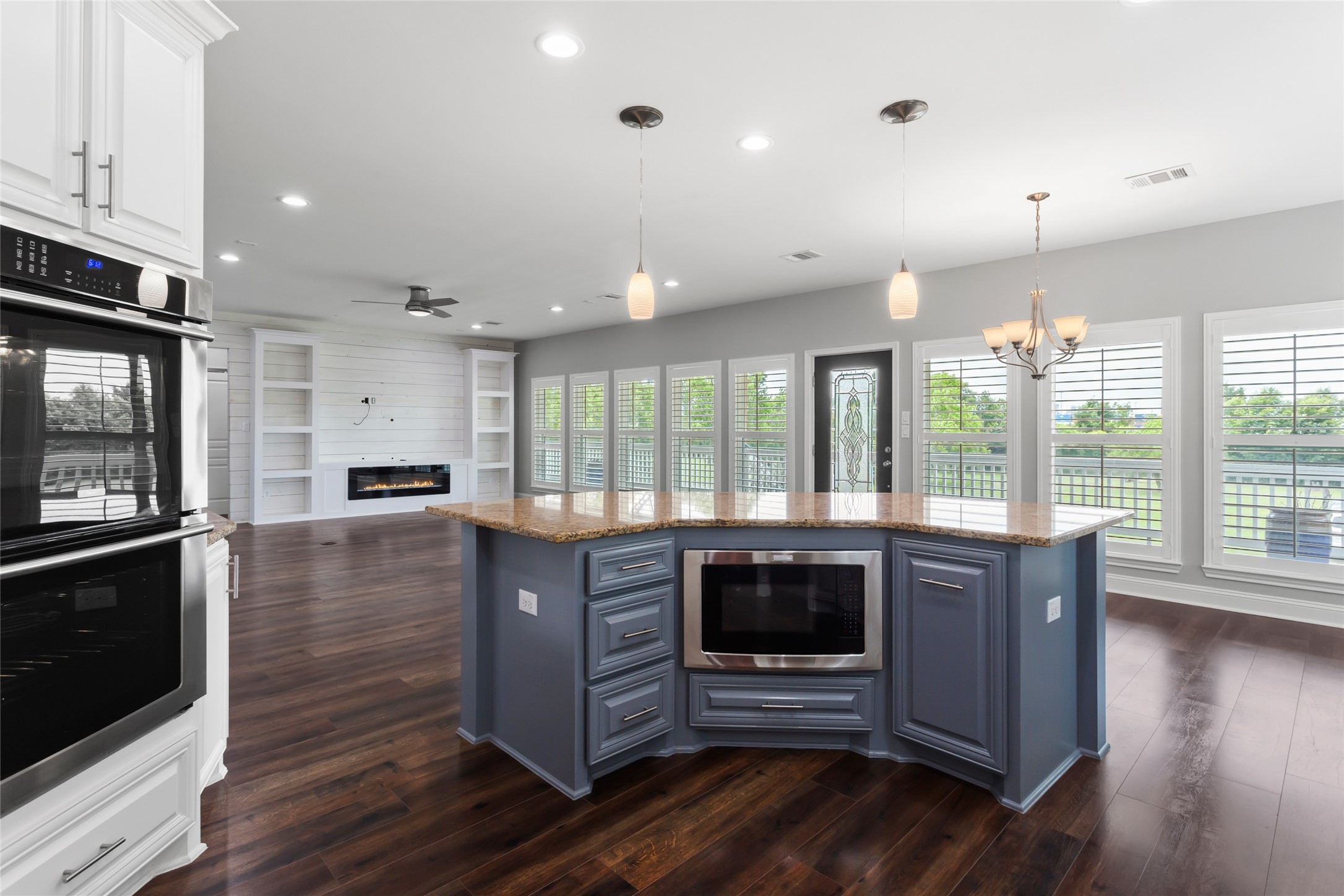 610 South Shady Lane La Porte, TX 77571 - Photo 18 of 50 This spacious, open-concept kitchen features a large island with a built-in microwave, modern pendant lighting, and ample natural light from large windows. The adjacent living area boasts a cozy fireplace and built-in shelving, all complemented by elegant wood laminate floors.