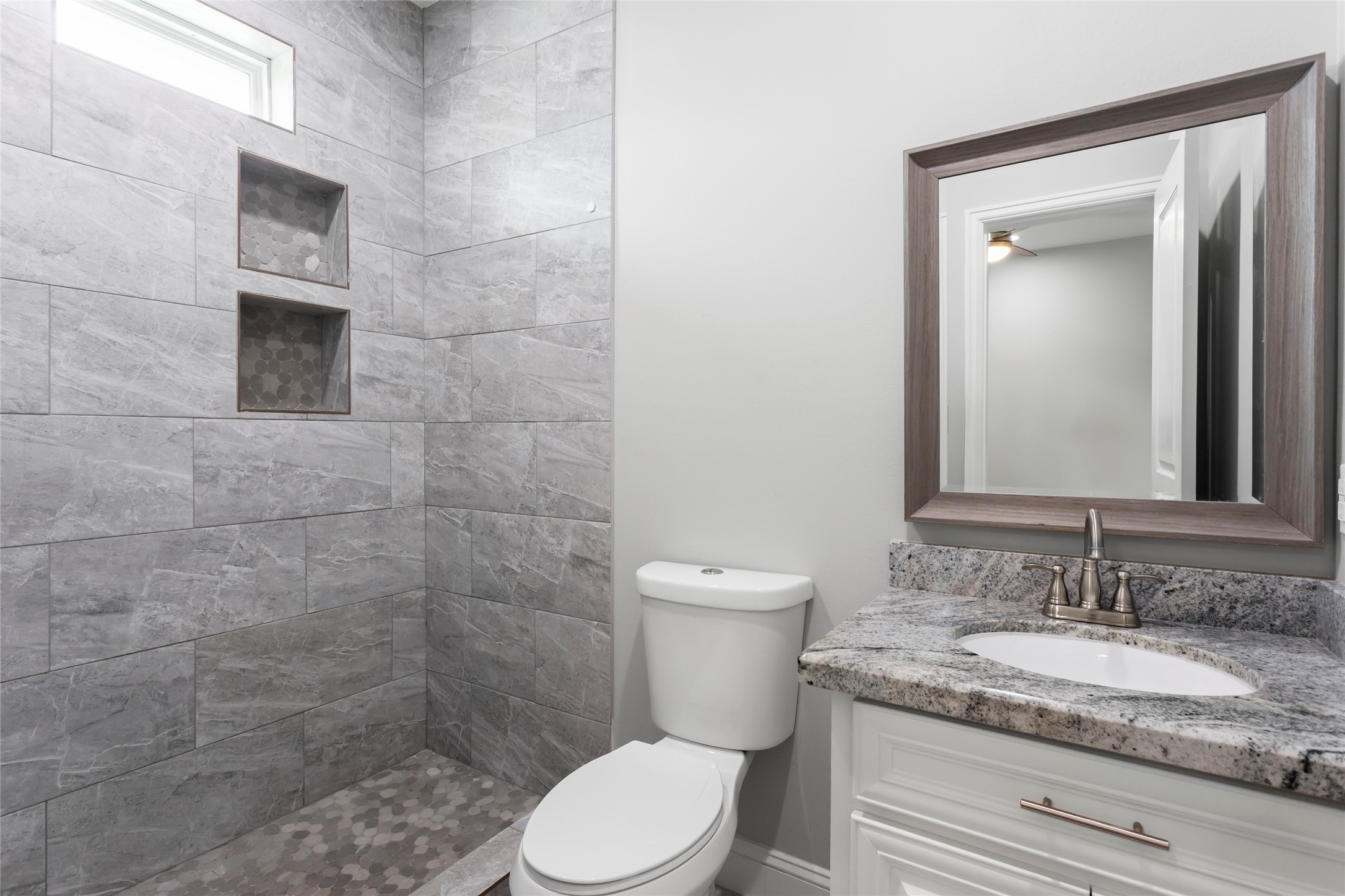 610 South Shady Lane La Porte, TX 77571 - Photo 25 of 50 This bathroom features a modern design with a sleek gray-tiled walk-in shower, built-in shelves, and a granite countertop vanity. The neutral color palette enhances the clean, contemporary feel.