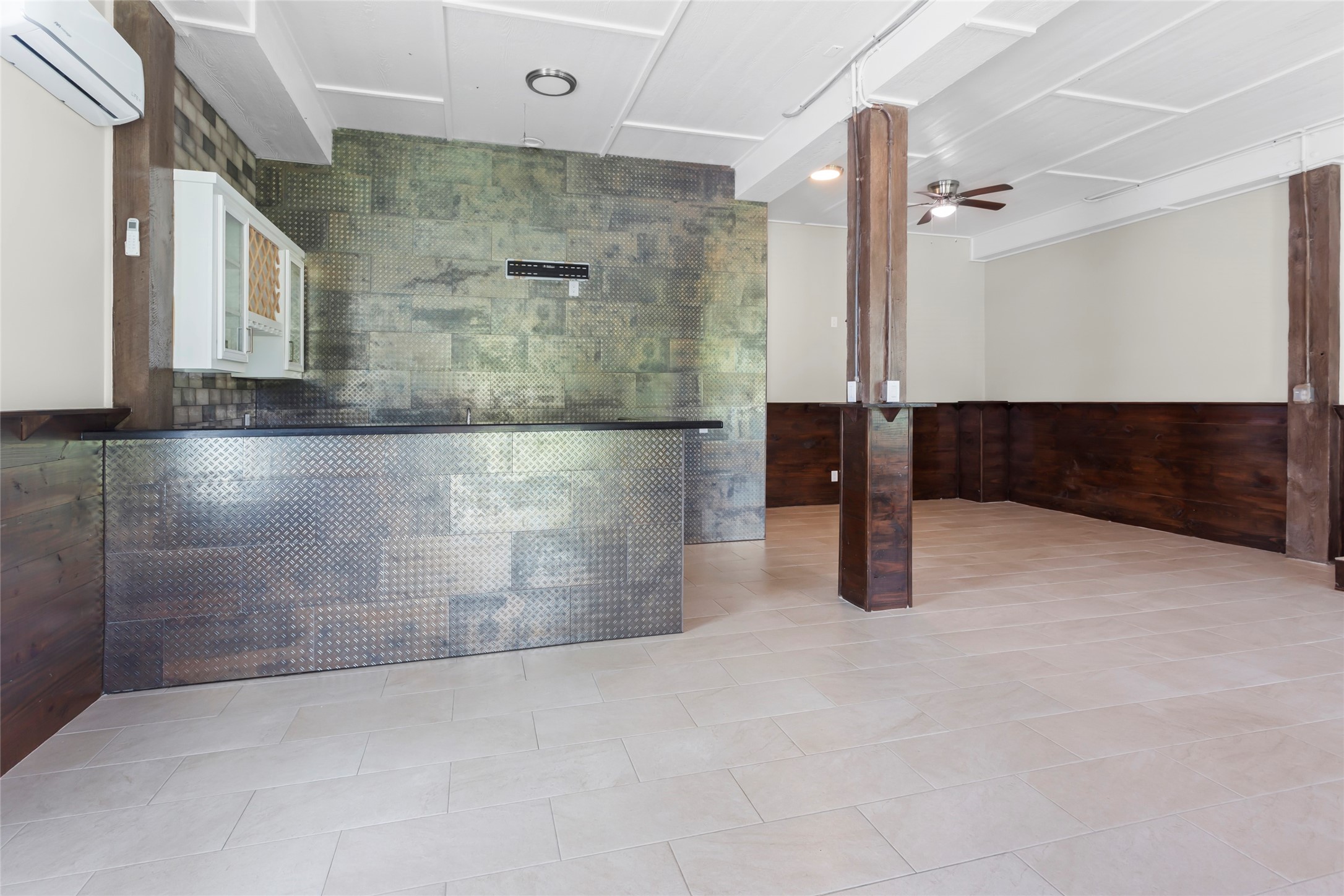 610 South Shady Lane La Porte, TX 77571 - Photo 31 of 50 This photo showcases the entrance into the downstairs unit. It's a spacious, modern room with light tile flooring, wood accents, and a metallic textured bar area. It features a ceiling fan, ample natural light, and an open layout, ideal for entertaining or versatile use.