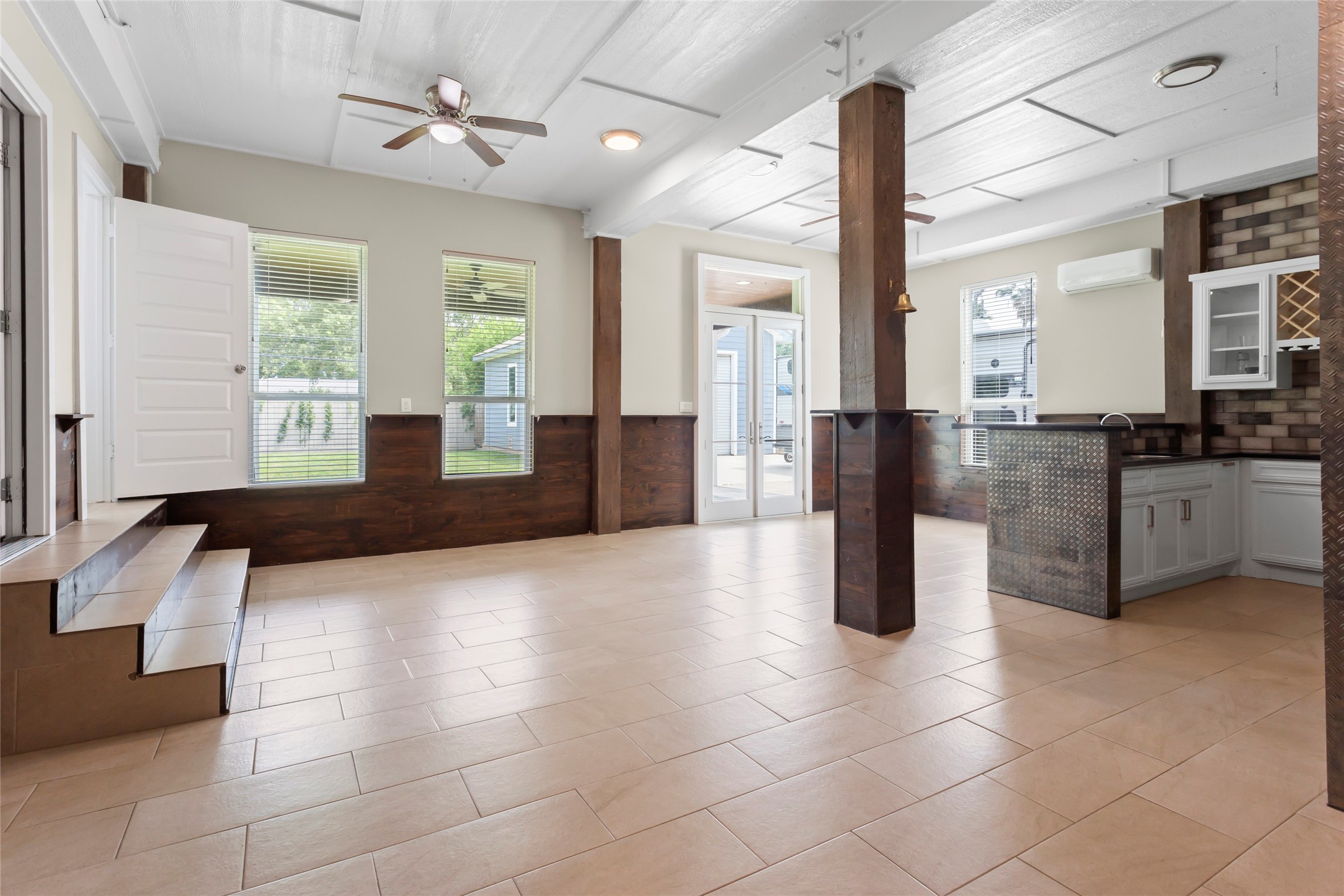 610 South Shady Lane La Porte, TX 77571 - Photo 34 of 50 This spacious open-concept room features large windows for natural light, a ceiling fan, modern tile flooring, and a unique blend of wood and brick accents. The area includes a step-up entry, a partial kitchen with a granite bar counter, and double doors leading outside, creating a versatile and inviting space.