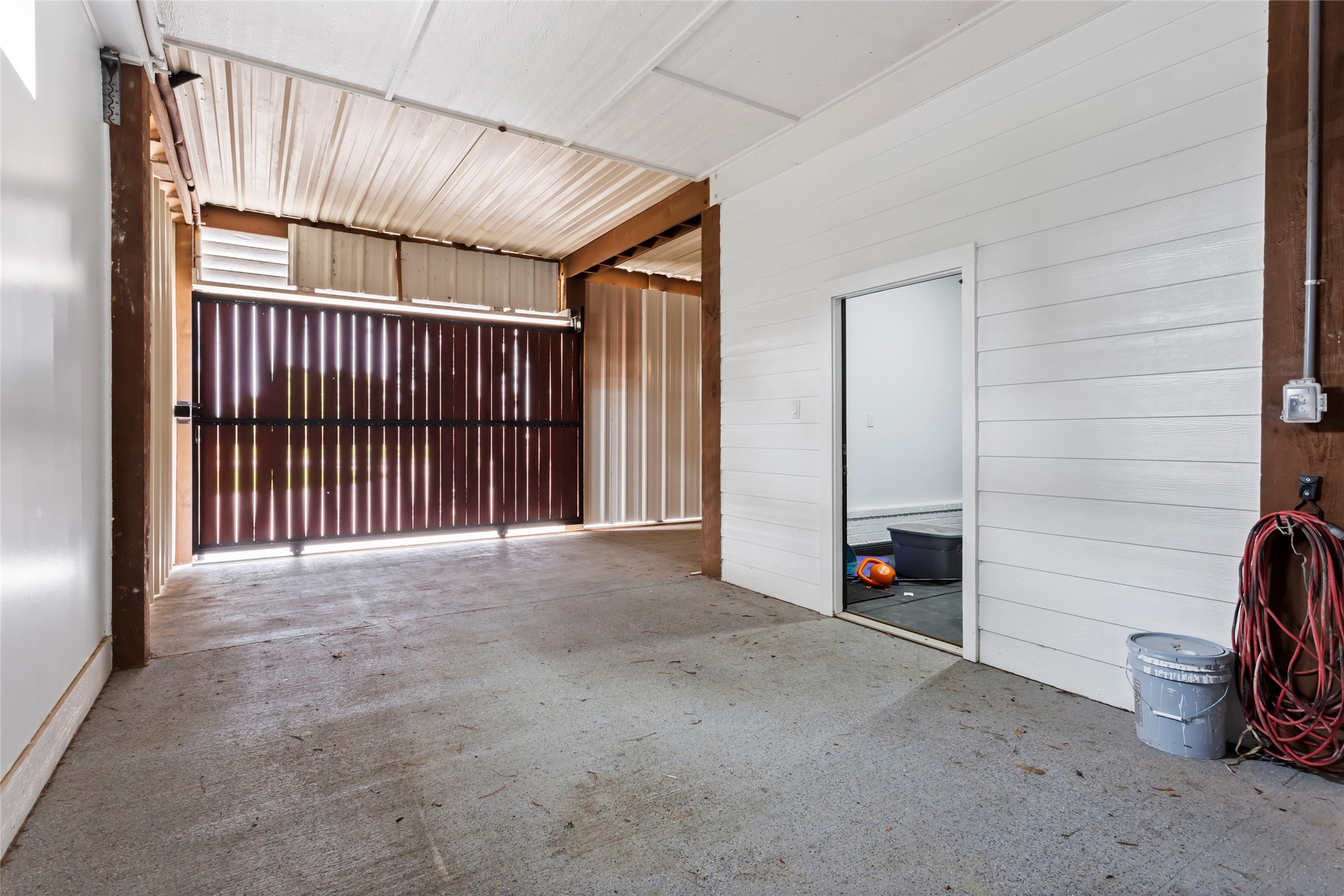 610 South Shady Lane La Porte, TX 77571 - Photo 44 of 50 This photo shows a spacious garage with a concrete floor and a large metal rolling door. The walls have a mix of painted paneling and exposed wood beams. There's an interior door leading to another room, and the space has ample natural light. Perfect for parking or storage.