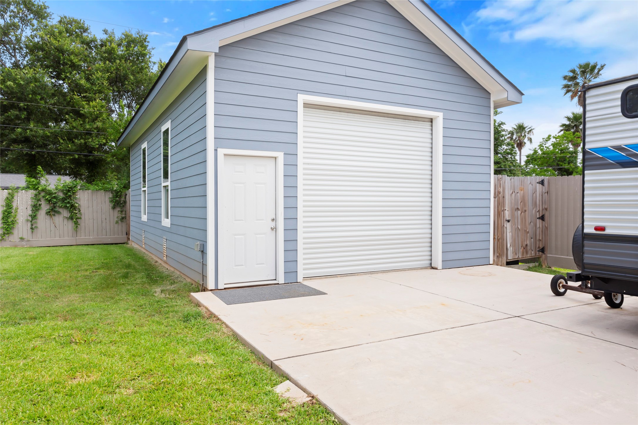 610 South Shady Lane La Porte, TX 77571 - Photo 47 of 50 This photo shows a well-maintained detached garage with blue siding, a white roll-up door, and a side entry door. The area features a concrete driveway and a fenced backyard, providing ample space for parking or storage.
