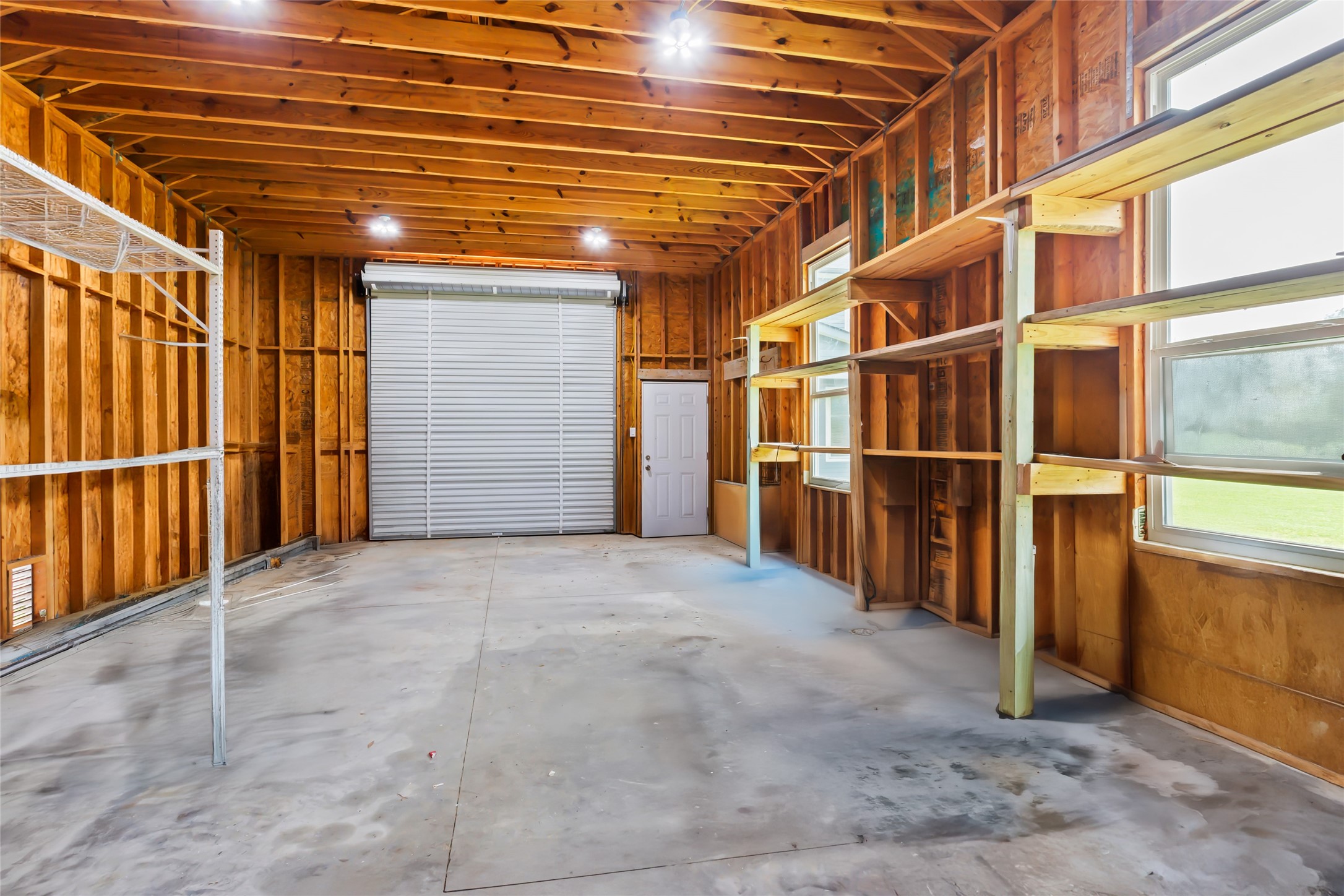 610 South Shady Lane La Porte, TX 77571 - Photo 48 of 50 This spacious garage features exposed wooden beams and ample shelving, with a large roll-up door and natural light from multiple windows—ideal for storage or a workshop.