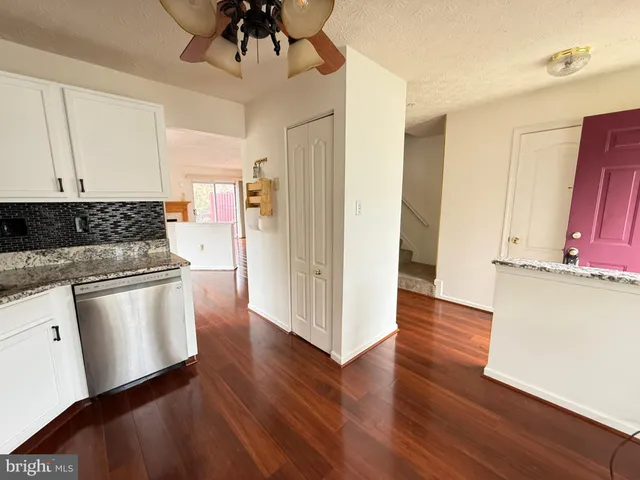 a kitchen with granite countertop a refrigerator a stove a sink and white cabinets with wooden floor