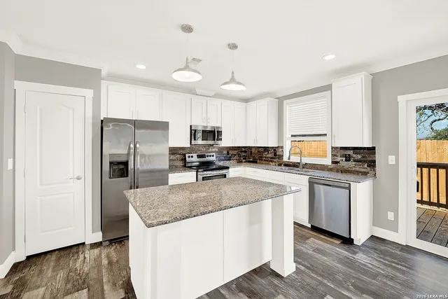 a kitchen with stainless steel appliances granite countertop a refrigerator a sink dishwasher a stove and white cabinets with wooden floor