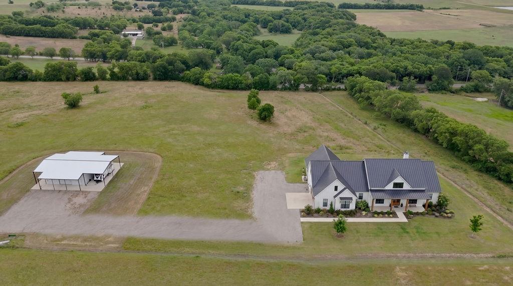 1161 Alsdorf Road Ennis, TX 75119 - Photo 19 of 28 Contemporary farmhouse-style residence featuring a dark metal roof, light-colored exterior, and an expansive gravel driveway