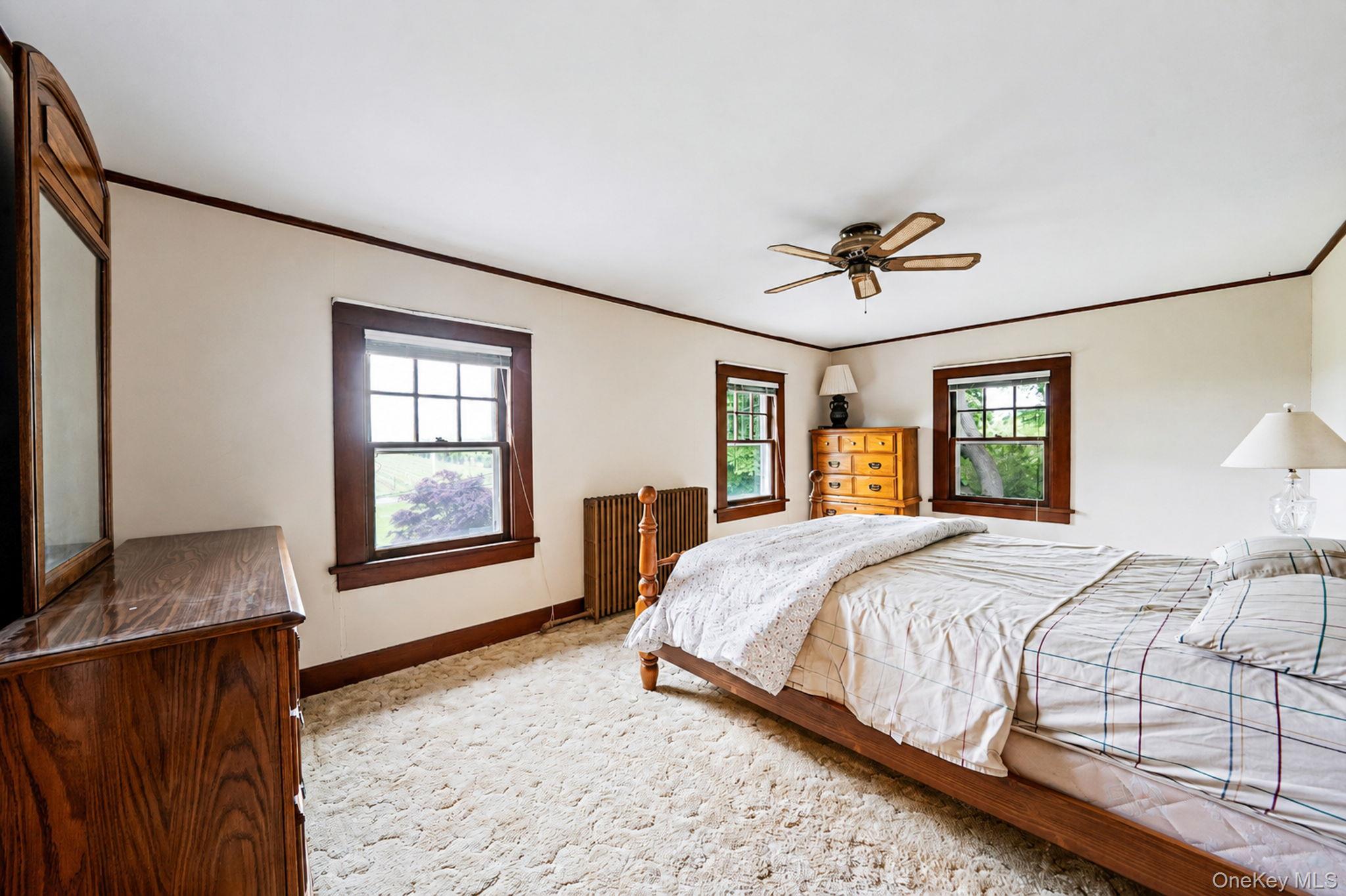 1055 Oregon Road Mattituck, NY 11952 - Photo 21 of 33 Spacious room featuring multiple windows with wood trim, ceiling fan, and light-colored carpeting. Wood floors under the carpeting.