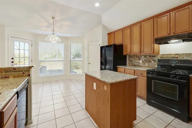 a kitchen with kitchen island granite countertop a stove top oven a sink dishwasher and a refrigerator with wooden cabinets