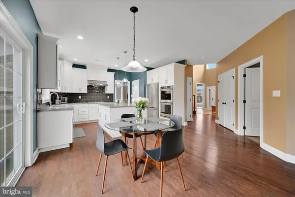 a kitchen with stainless steel appliances kitchen island granite countertop a refrigerator a stove a sink a dining table and chairs with wooden floor