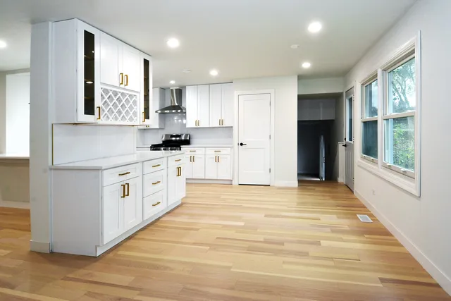 a large white kitchen with stainless steel appliances granite countertop a large stove a sink and white cabinets with wooden floor