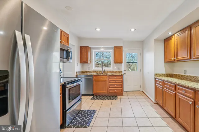 a kitchen with stainless steel appliances granite countertop a refrigerator a sink dishwasher a stove and white countertops with wooden floor