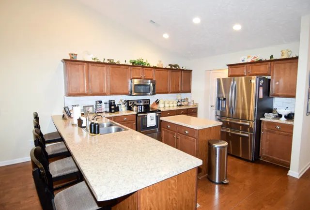 a large kitchen with stainless steel appliances kitchen island granite countertop a refrigerator a stove a sink a dining table and chairs with wooden floor