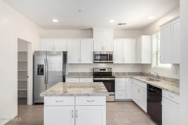 a kitchen with stainless steel appliances granite countertop a refrigerator a stove a sink and white cabinets