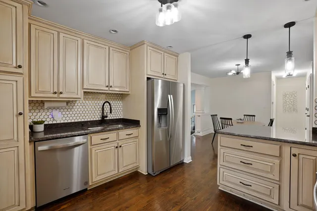 a kitchen with granite countertop a refrigerator a sink dishwasher a oven and white cabinets with wooden floor