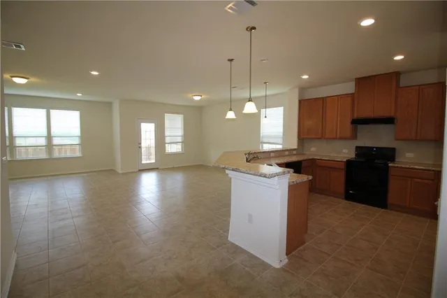 a kitchen with a stove a sink a center island a counter top space and cabinets