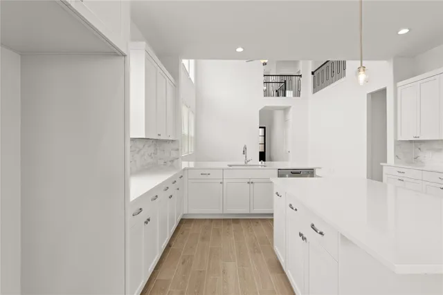 a large white kitchen with granite countertop a sink and dishwasher a refrigerator with white cabinets