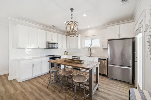 a kitchen with stainless steel appliances granite countertop a refrigerator a sink dishwasher a stove and white cabinets with wooden floor