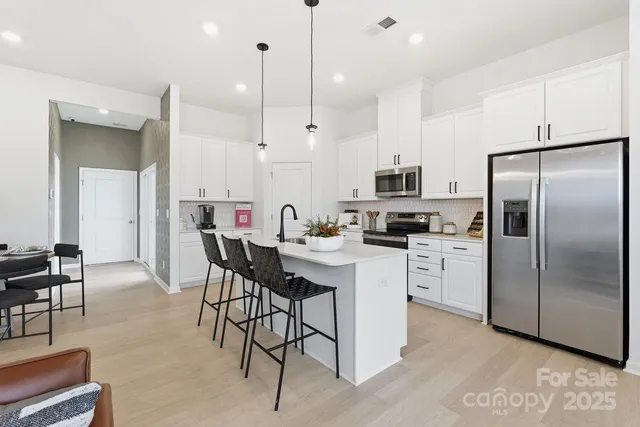 a kitchen with stainless steel appliances kitchen island a white table chairs and a refrigerator