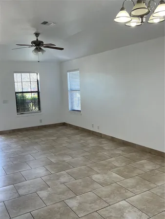 an empty room with a chandelier fan and windows
