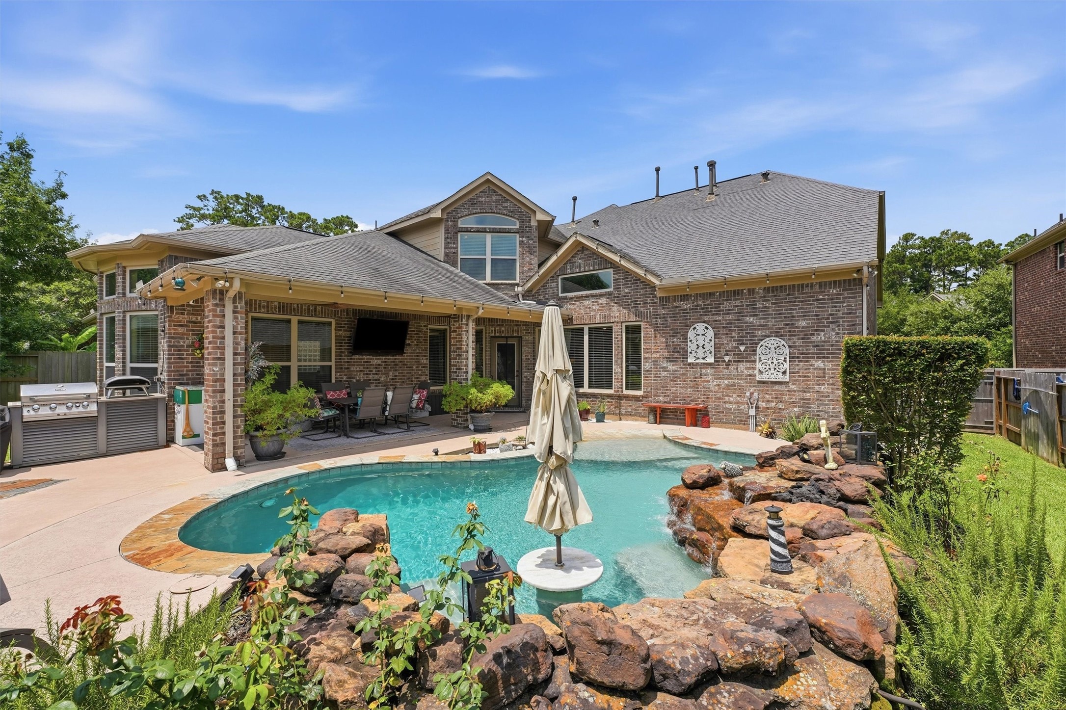 17710 Rough River Court Humble, TX 77346 - Photo 29 of 38 This backyard features a spacious in-ground pool with a waterfall, surrounded by a stone patio. There are several seating areas with umbrellas, and the space is enclosed by a wooden fence, offering privacy and a great spot for relaxation or entertaining.