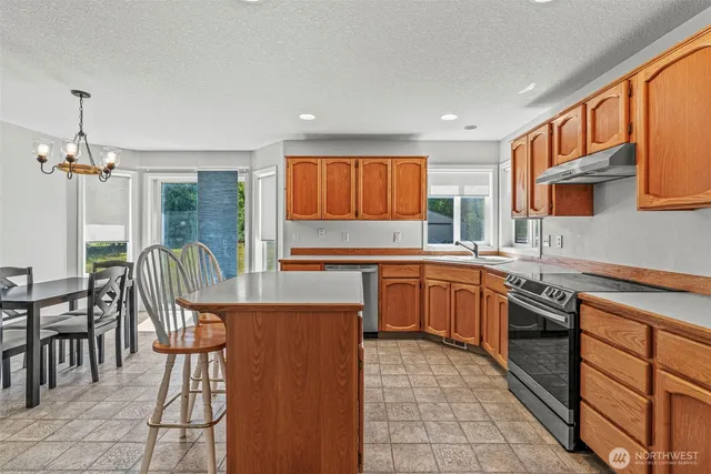 a kitchen with stainless steel appliances granite countertop a stove top oven a sink dishwasher a dining table and chairs with wooden floor